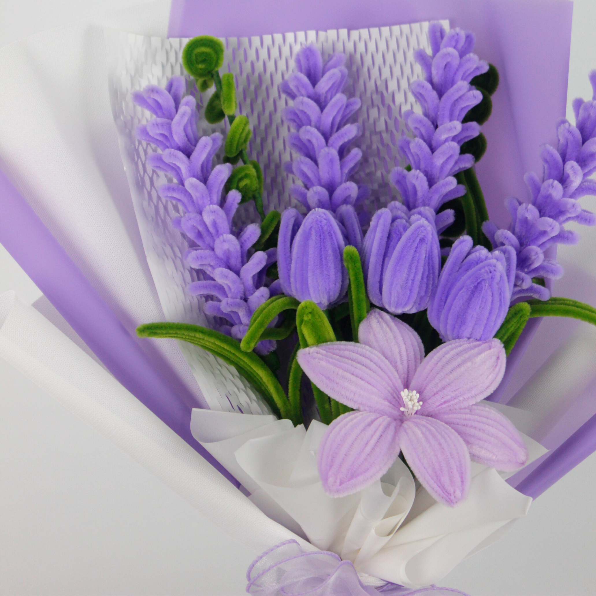 Bouquet of purple flowers wrapped in white paper with a purple ribbon on a light gray background