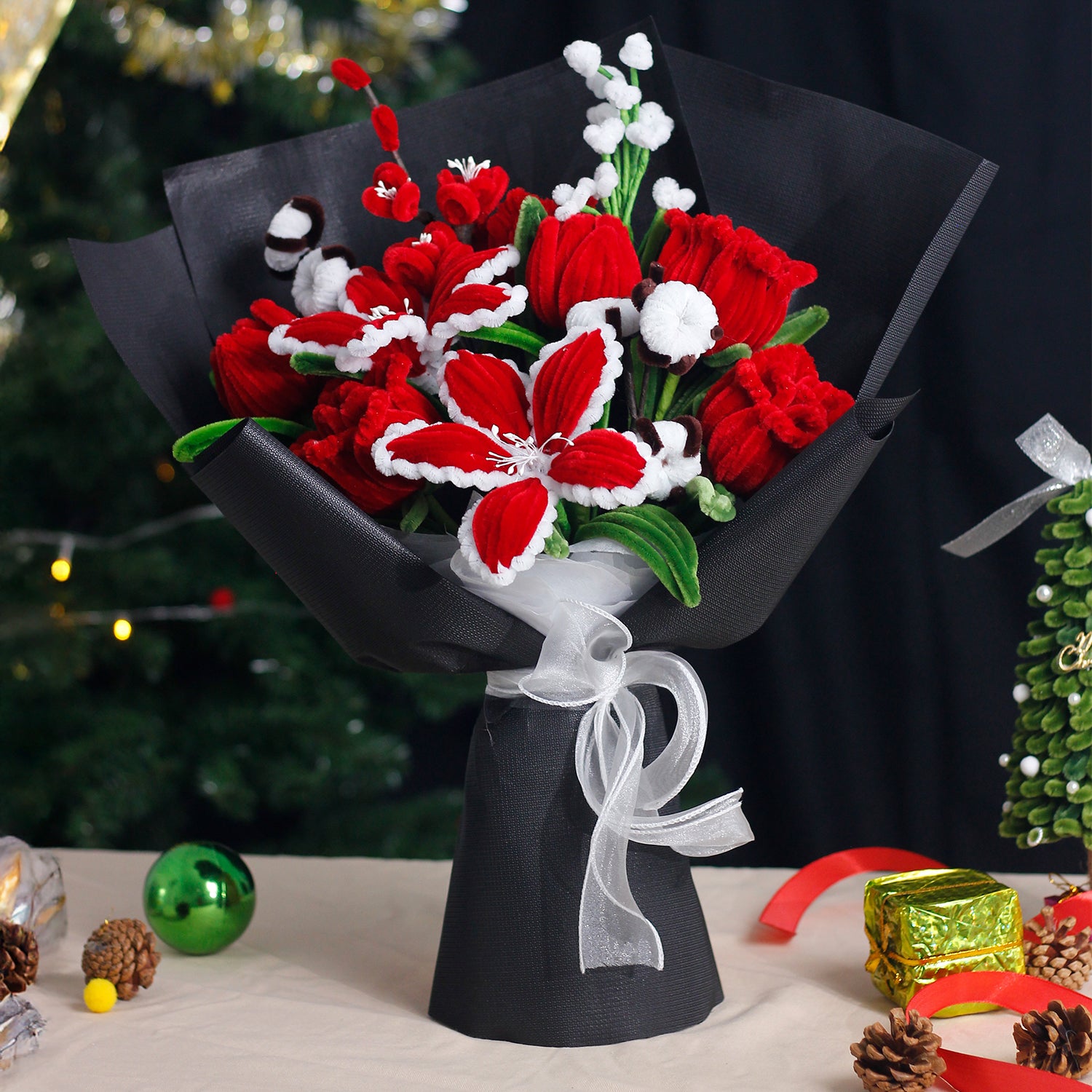 Red and white handmade pipe cleaner bouquet wrapped in festive Christmas paper with red bow. Features poinsettia-inspired flowers and snowflake accents. Ideal for holiday gifts.