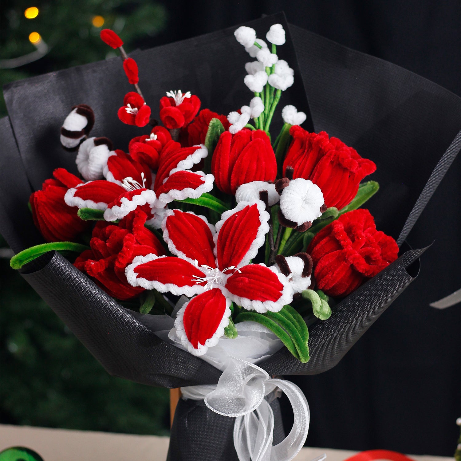 Red and white handmade pipe cleaner bouquet wrapped in festive Christmas paper with red bow. Features poinsettia-inspired flowers and snowflake accents. Ideal for holiday gifts.
