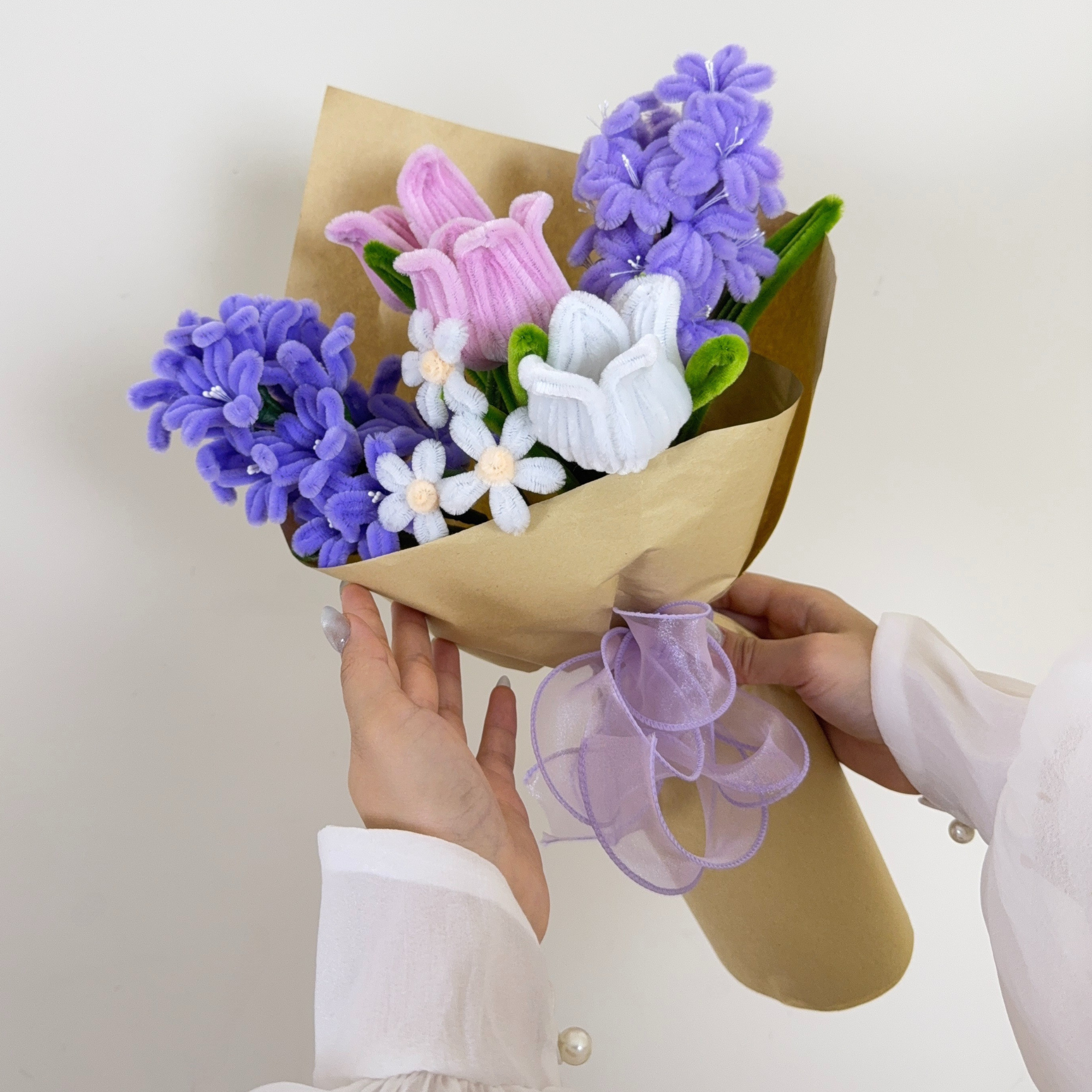 Bouquet of flowers wrapped in brown paper with a white ribbon on a light gray background