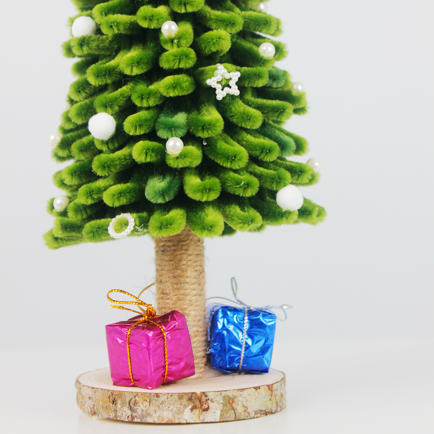 Handmade green pipe cleaner Christmas tree decorated with white pearls, silver bow, and "Merry Christmas" sign, displayed with pink and blue gift boxes on a wooden base — perfect for festive decor or gift.