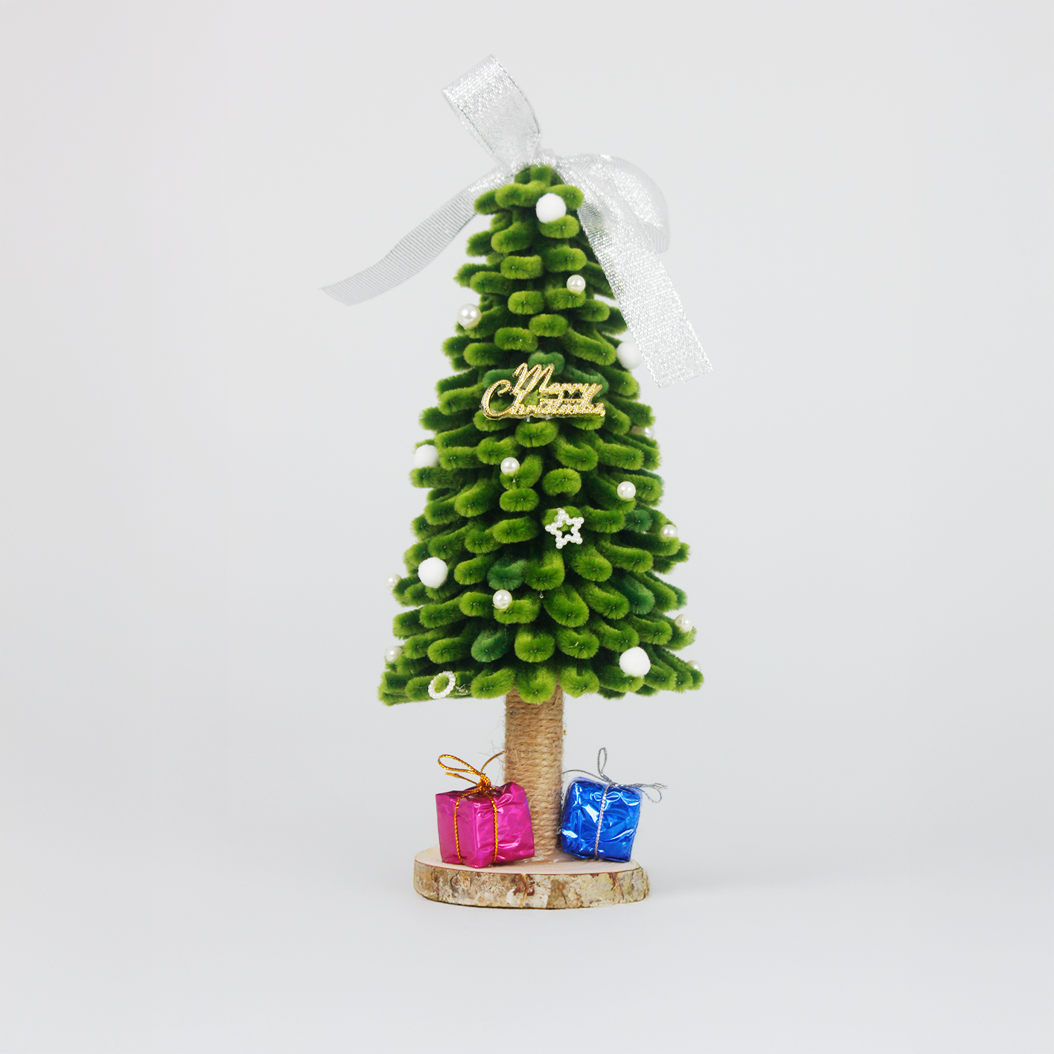 Handmade green pipe cleaner Christmas tree decorated with white pearls, silver bow, and "Merry Christmas" sign, displayed with pink and blue gift boxes on a wooden base — perfect for festive decor or gift.